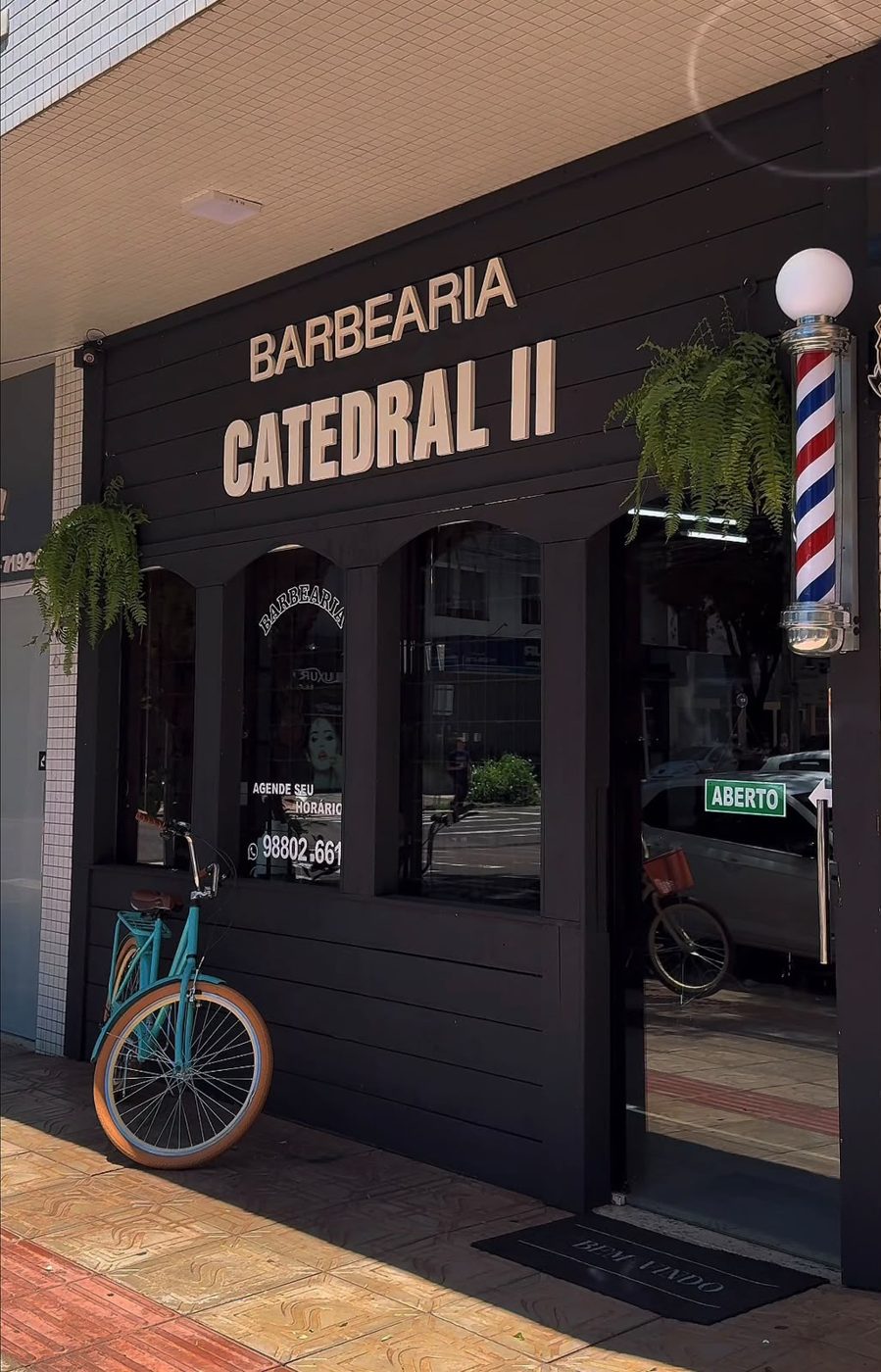 Fachada preta da Barbearia Catedral II com poste de barbeiro e bicicleta