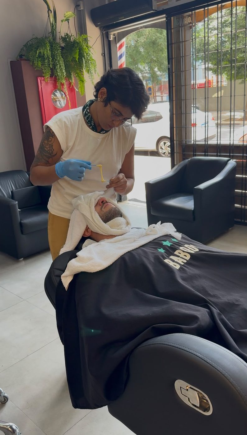 Kamilla atendendo um cliente na cadeira, de frente para a vitrine